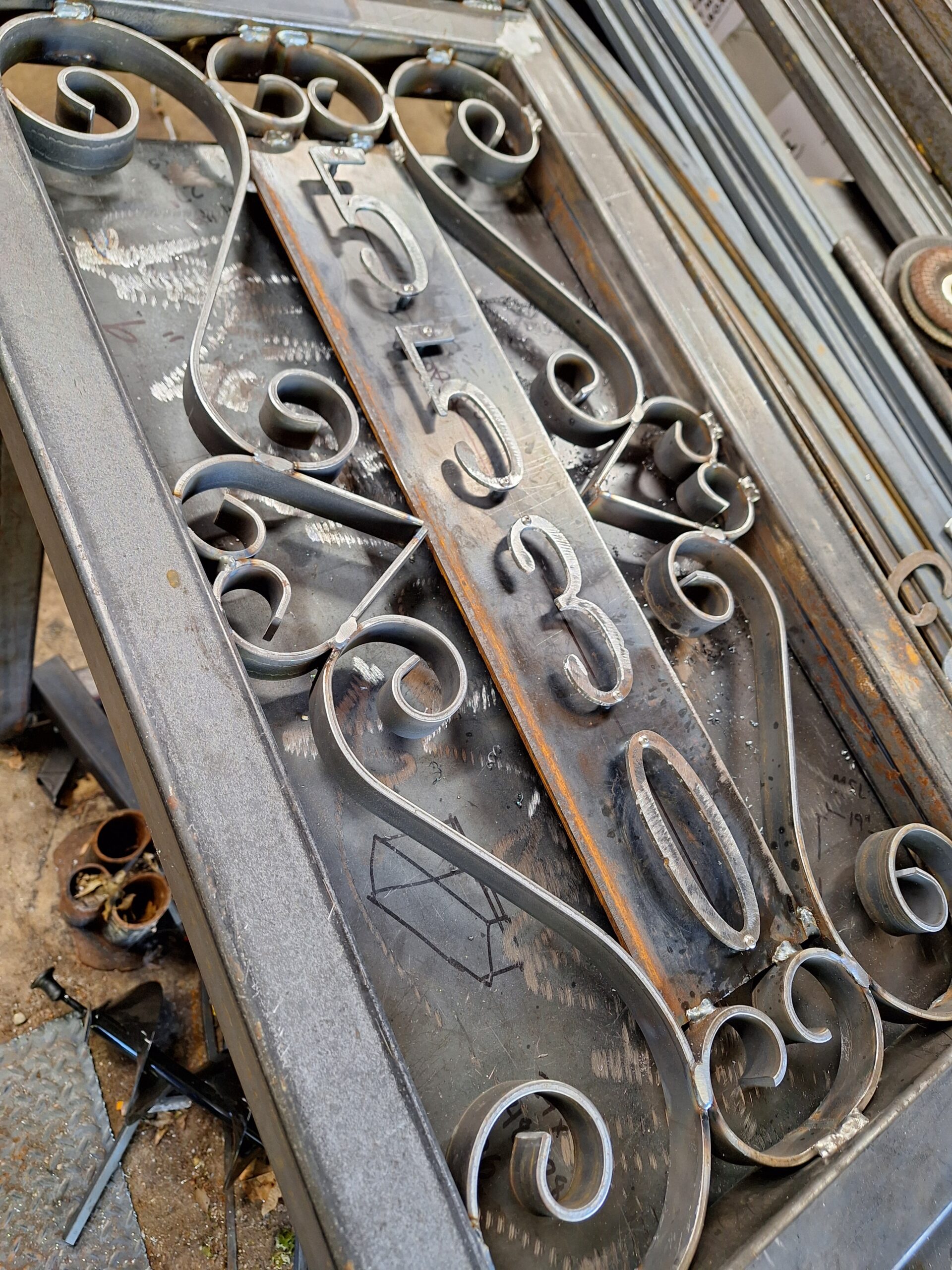 raw steel decorative mail box post.  decorative scroll work surrounds a number plate.  